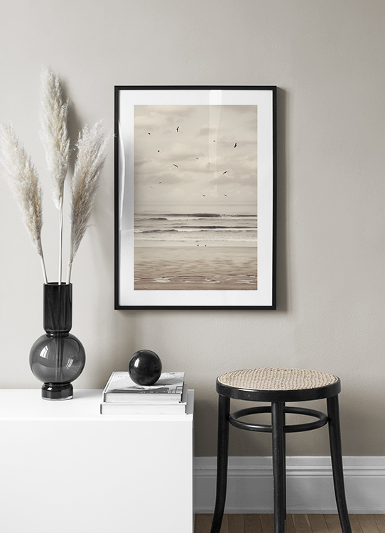  – Photographie d’une plage et d’un océan avec des oiseaux noirs volant devant un ciel nuageux