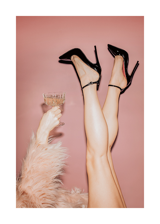  – Eine Frau in schwarzen High Heels und einem rosa Kunstpelzmantel, die ein Glas Champagner hält