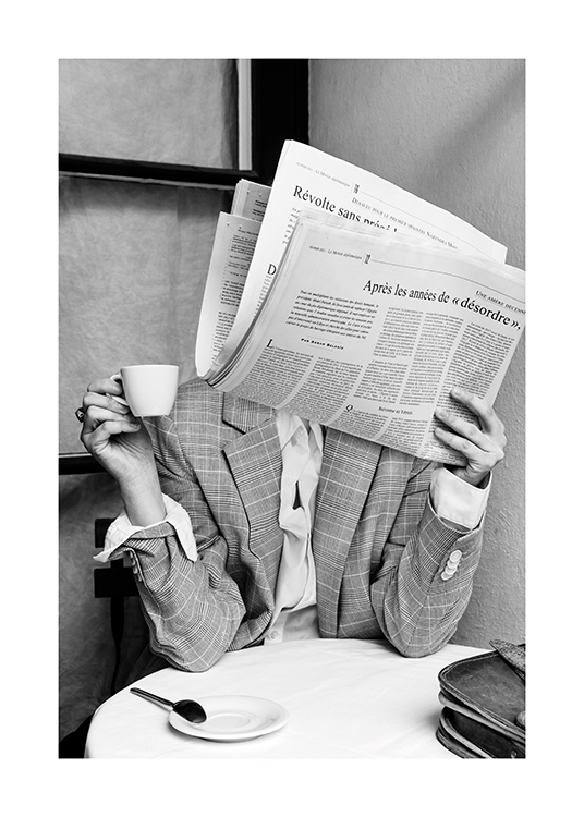  – Photographie en noir et blanc d’une personne assise à une table de café avec un journal couvrant son visage