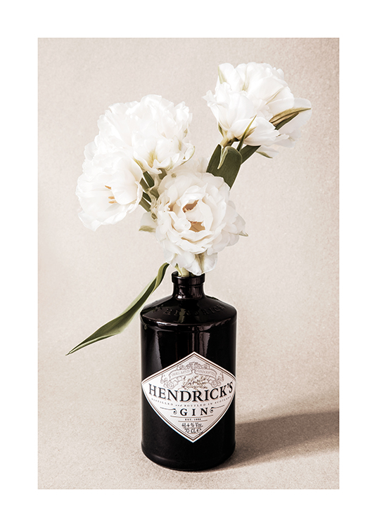  – Photographie d’un bouquet de fleurs blanches dans une bouteille de gin noire, sur un fond beige granuleux